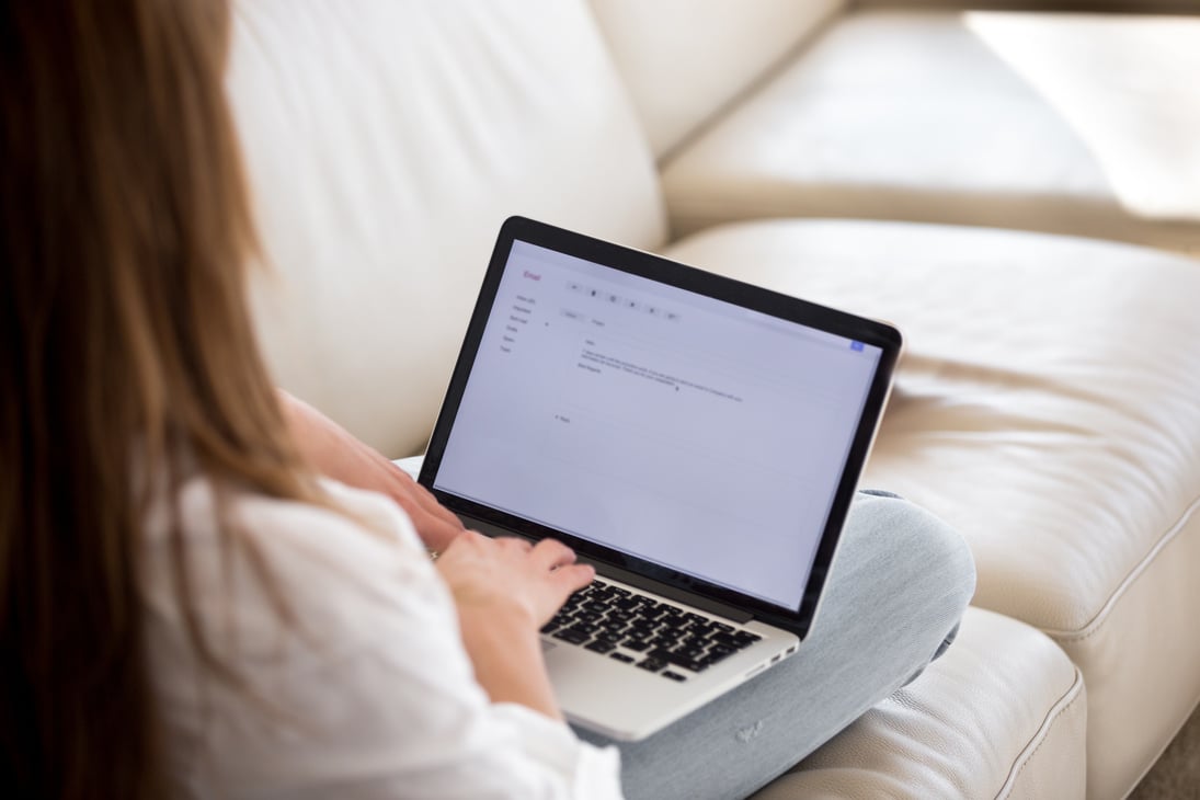 Rear view at woman writing email on laptop at home